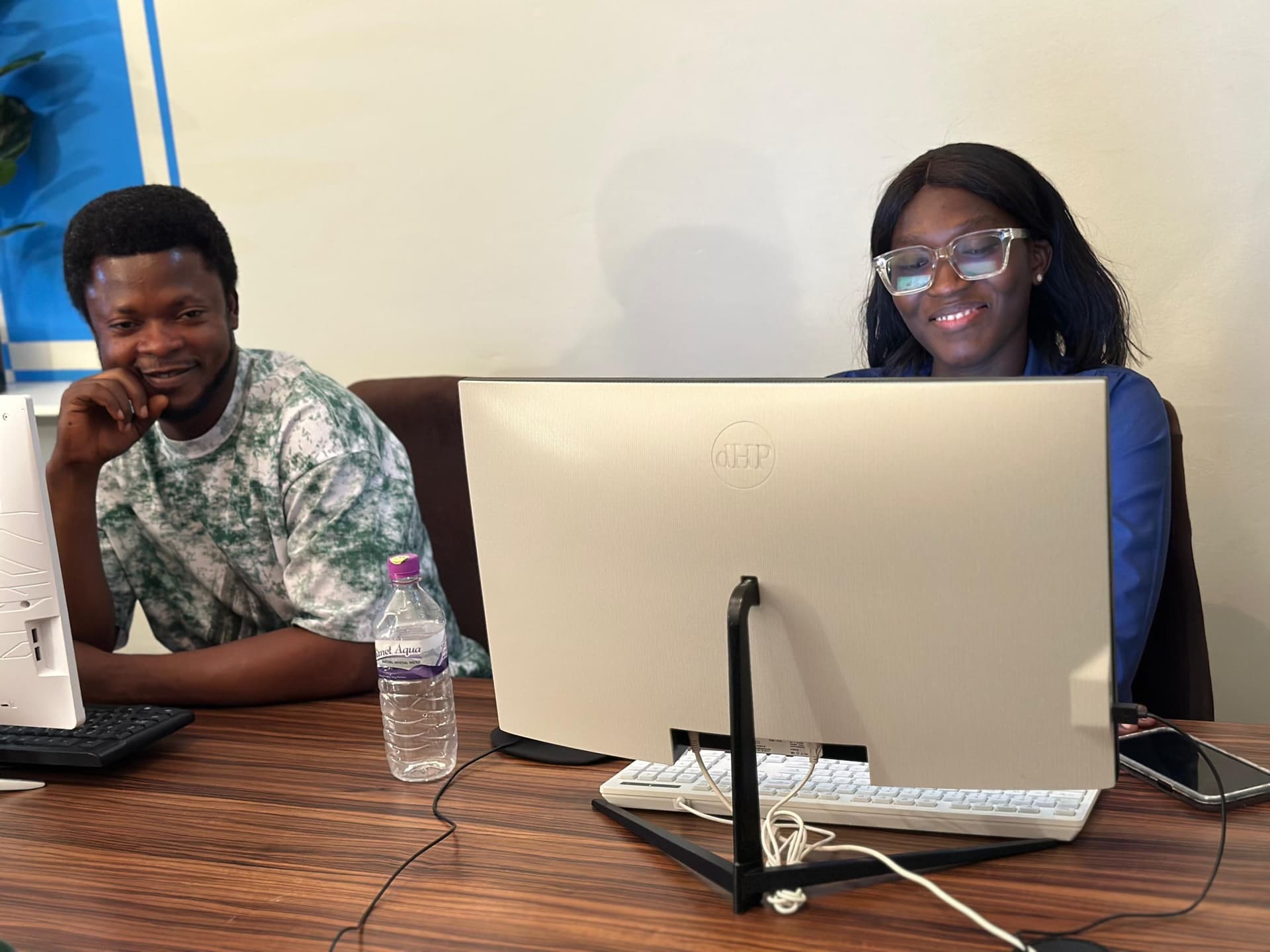 Two colleagues smiling at a shared desk with a desktop computer